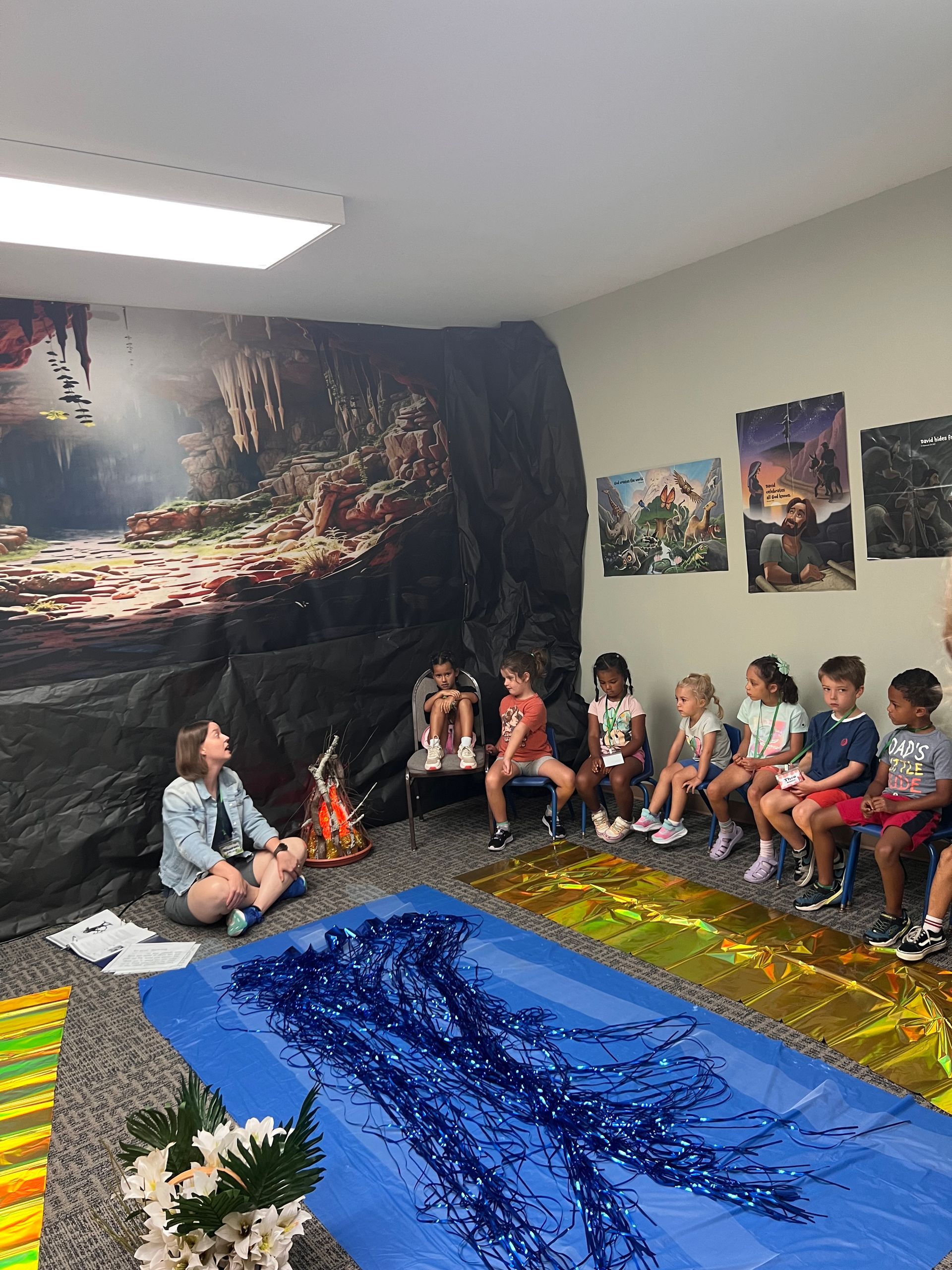Children seated in a classroom beside a blue tarp “river” and colorful nature backdrop