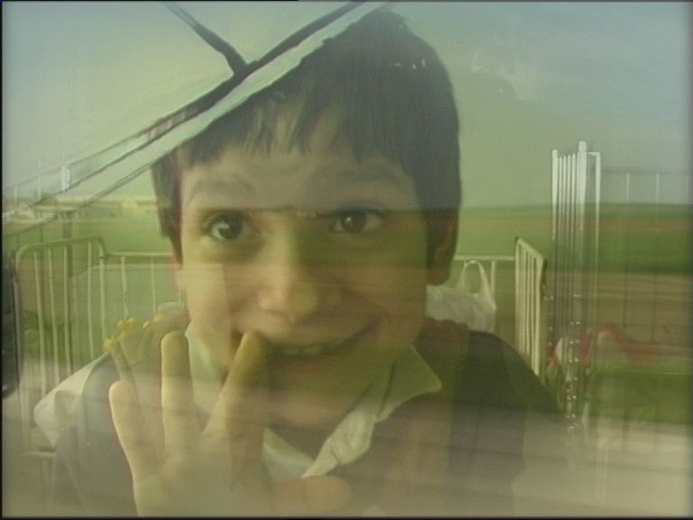 Child smiling and waving through a window, with a green field in the background