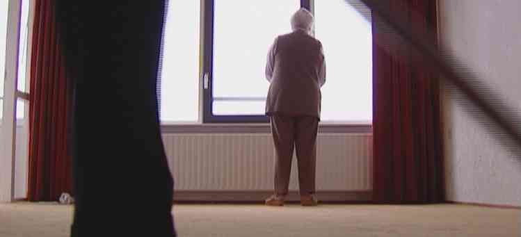 Person standing by a large bright window in a room with red curtains