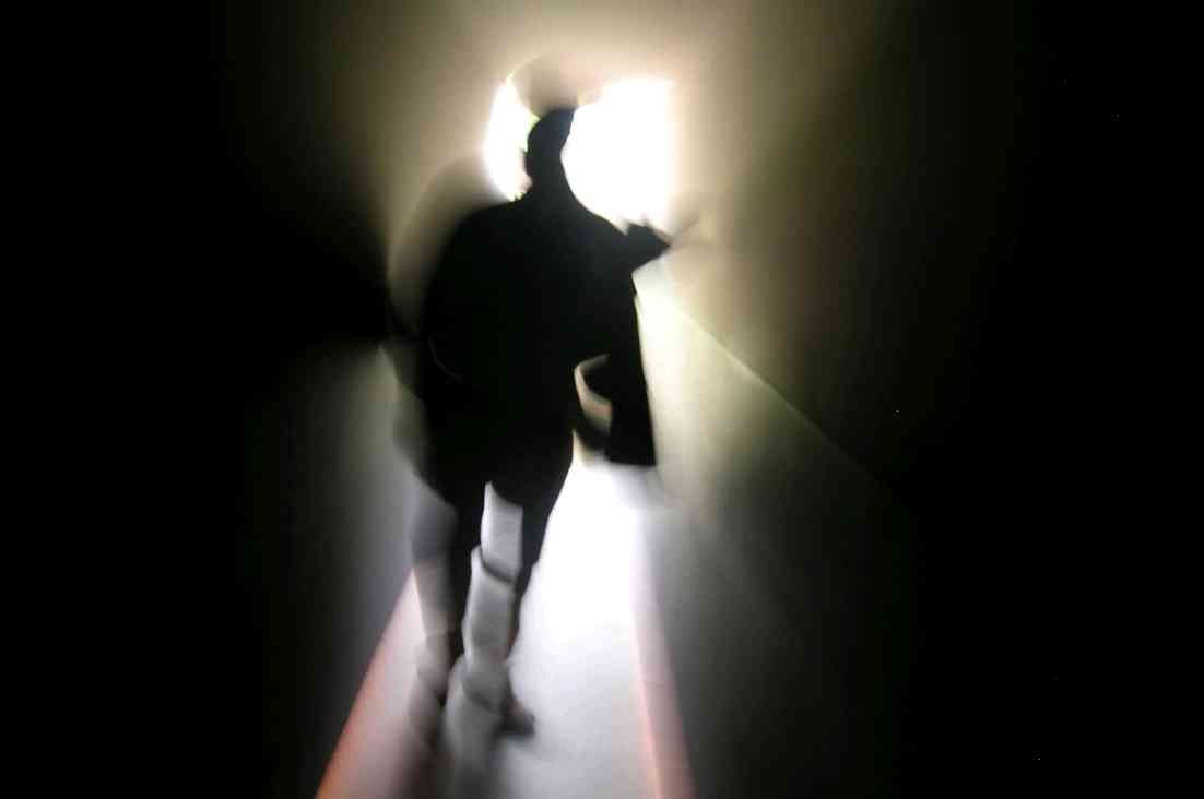 Silhouette of a person walking through a bright, narrow tunnel toward light