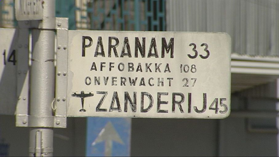 Street sign listing Paranam, Afobaka, Onverwacht, and Zanderij with distances.