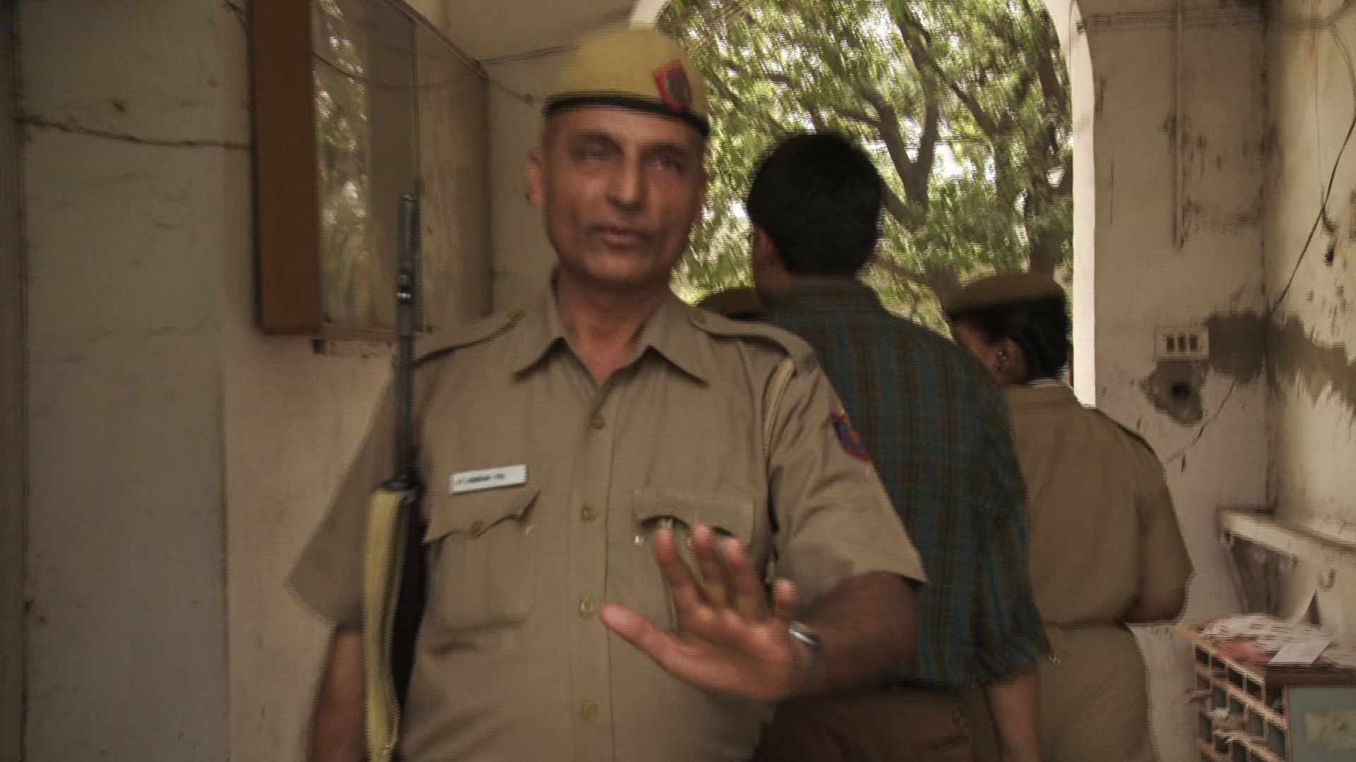 Uniformed officer stands at a doorway, holding up a hand, with two people walking away behind him.