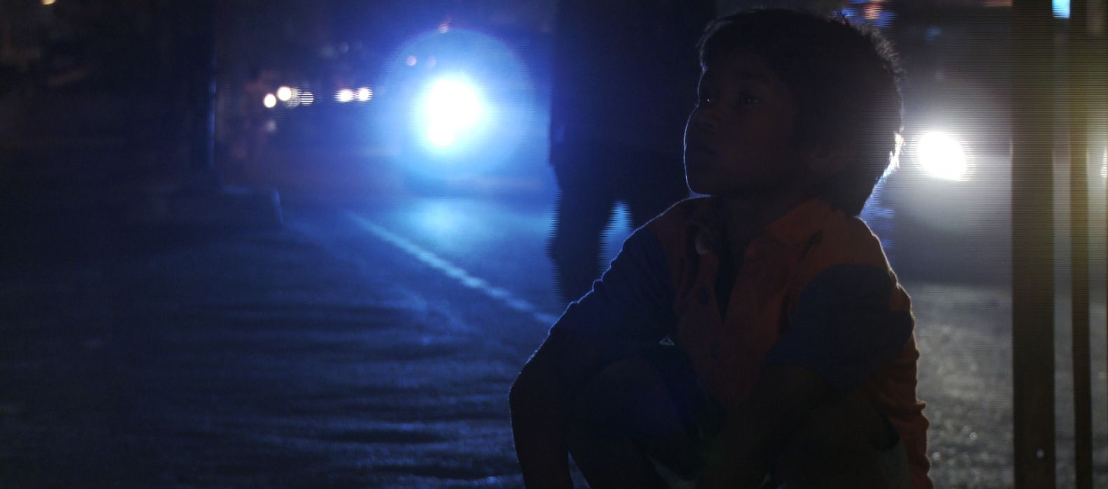 Person silhouetted at night beside bright headlights on a dark road