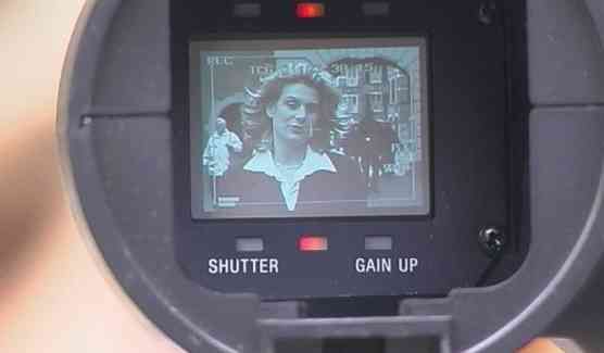 Camera viewfinder showing a woman indoors, with SHUTTER and GAIN UP labels visible