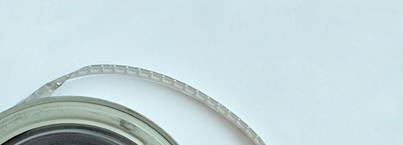 Close-up of a metal bottle cap against a pale blue background, with a curved transparent tube or strap