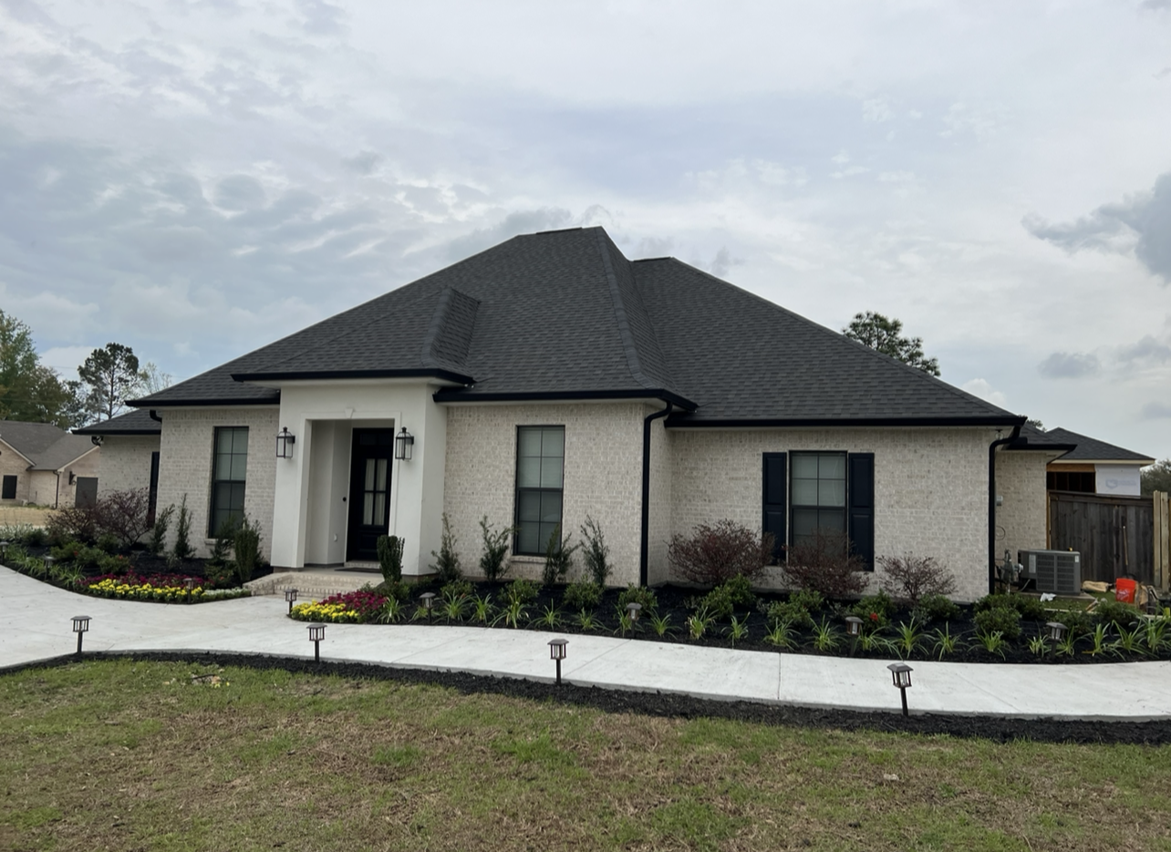 A large white house with a black roof and a driveway leading to it.