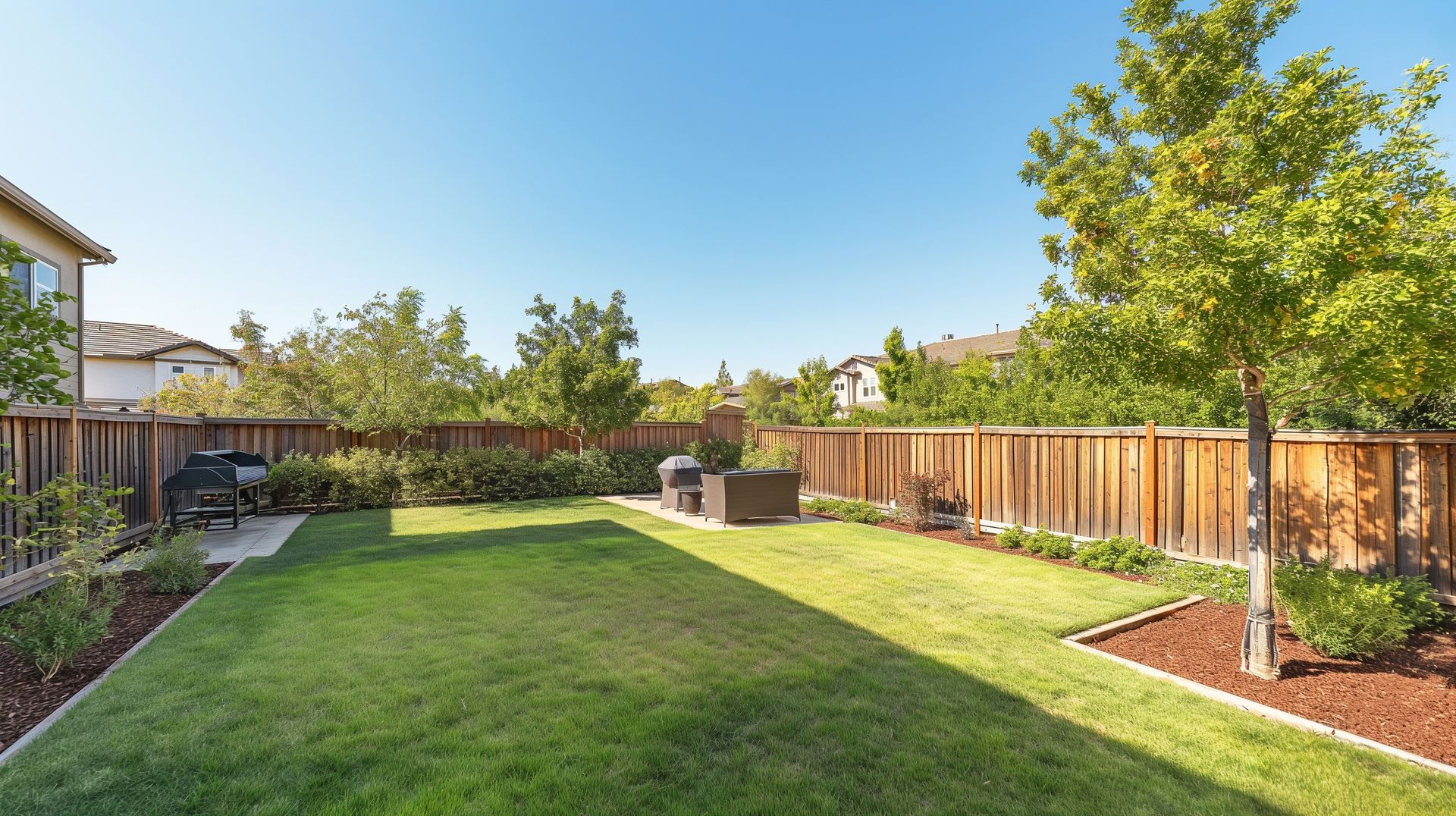 A backyard with a wooden fence and a lush green lawn.