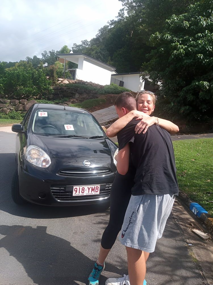 Two People Hugging In Front Of A Car With License — Solitude Driving School In Mooroobool, QLD