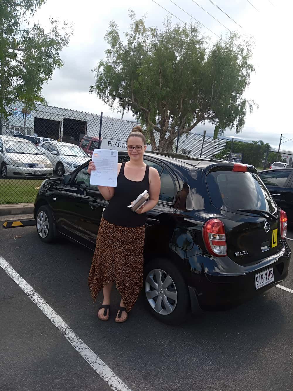 A Woman Is Standing In Front Of A Black Car In A Parking — Solitude Driving School In Mooroobool, QLD