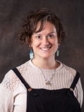A woman wearing overalls and a sweater is smiling for the camera.