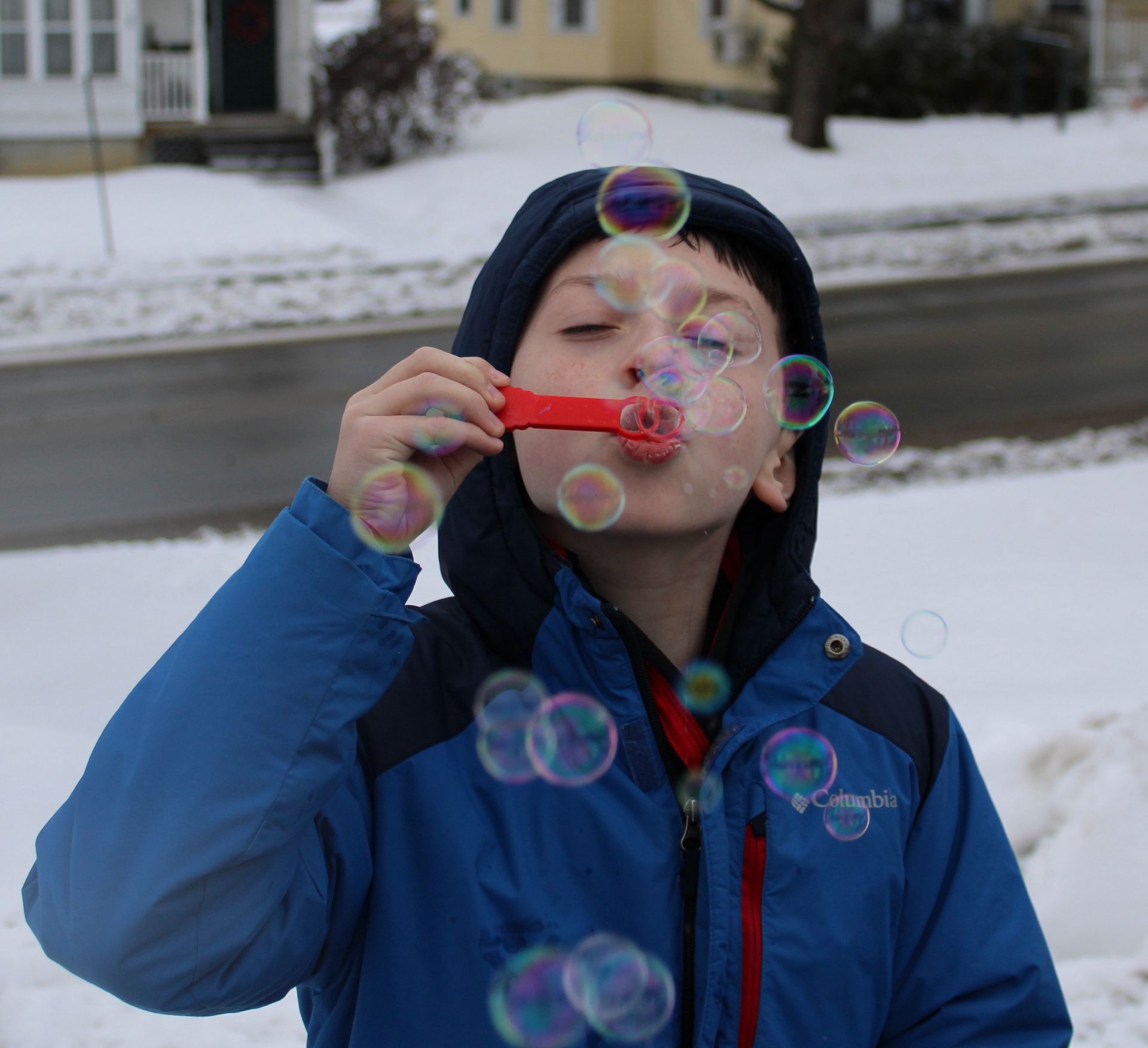 A young boy blowing soap bubbles in the snow