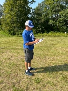 A man is standing in a field holding a clipboard.