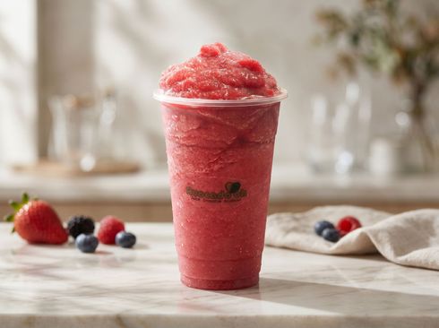 Red strawberry slush in a clear cup on a wooden table with fresh berries nearby