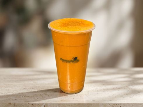 Orange smoothie in a clear plastic cup on a table, with a blurred background
