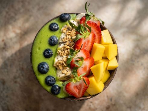 Overhead view of a smoothie bowl topped with blueberries, strawberries, granola, and mango cubes