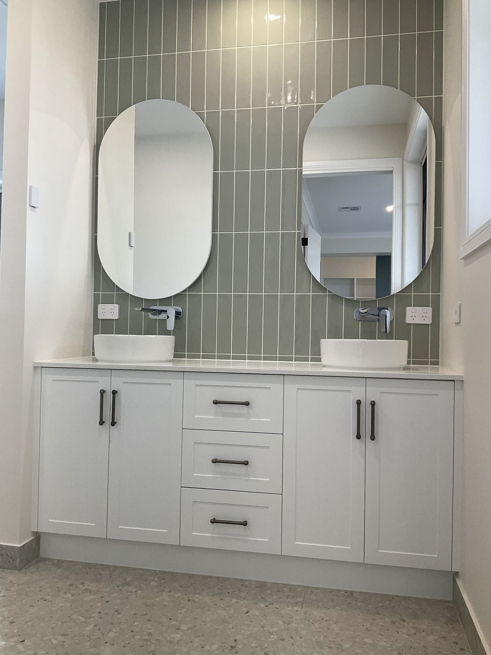 Bathroom vanity with two oval mirrors, white cabinets, and grey tile backsplash — Twomey Homes in Delacombe, VIC