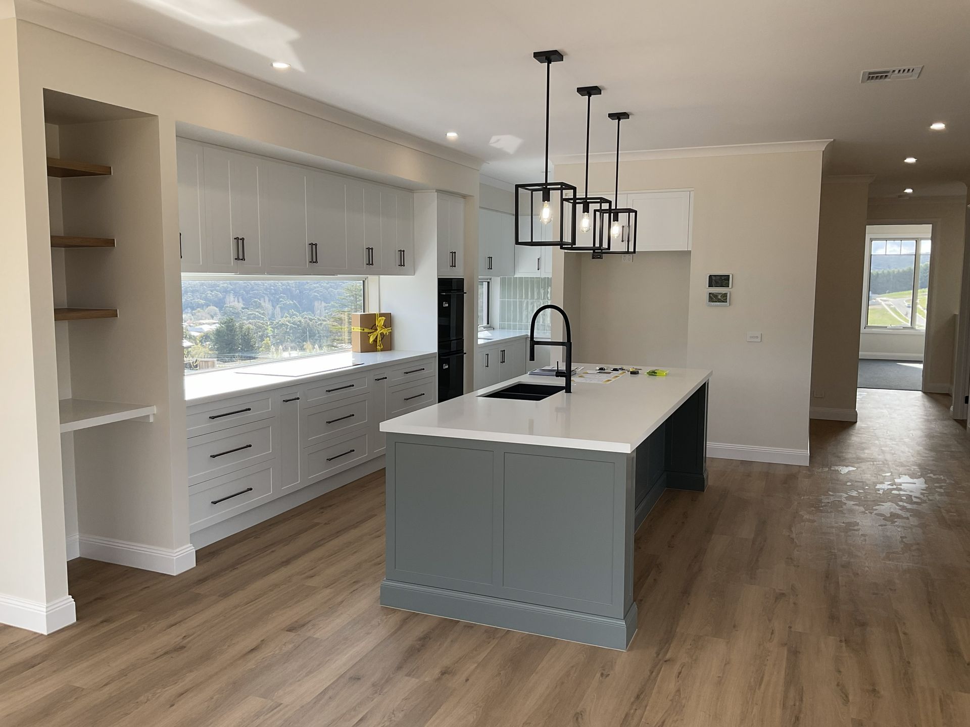 Bright modern kitchen with large island, black fixtures, white cabinets, and wood floors — Twomey Homes in Delacombe, VIC