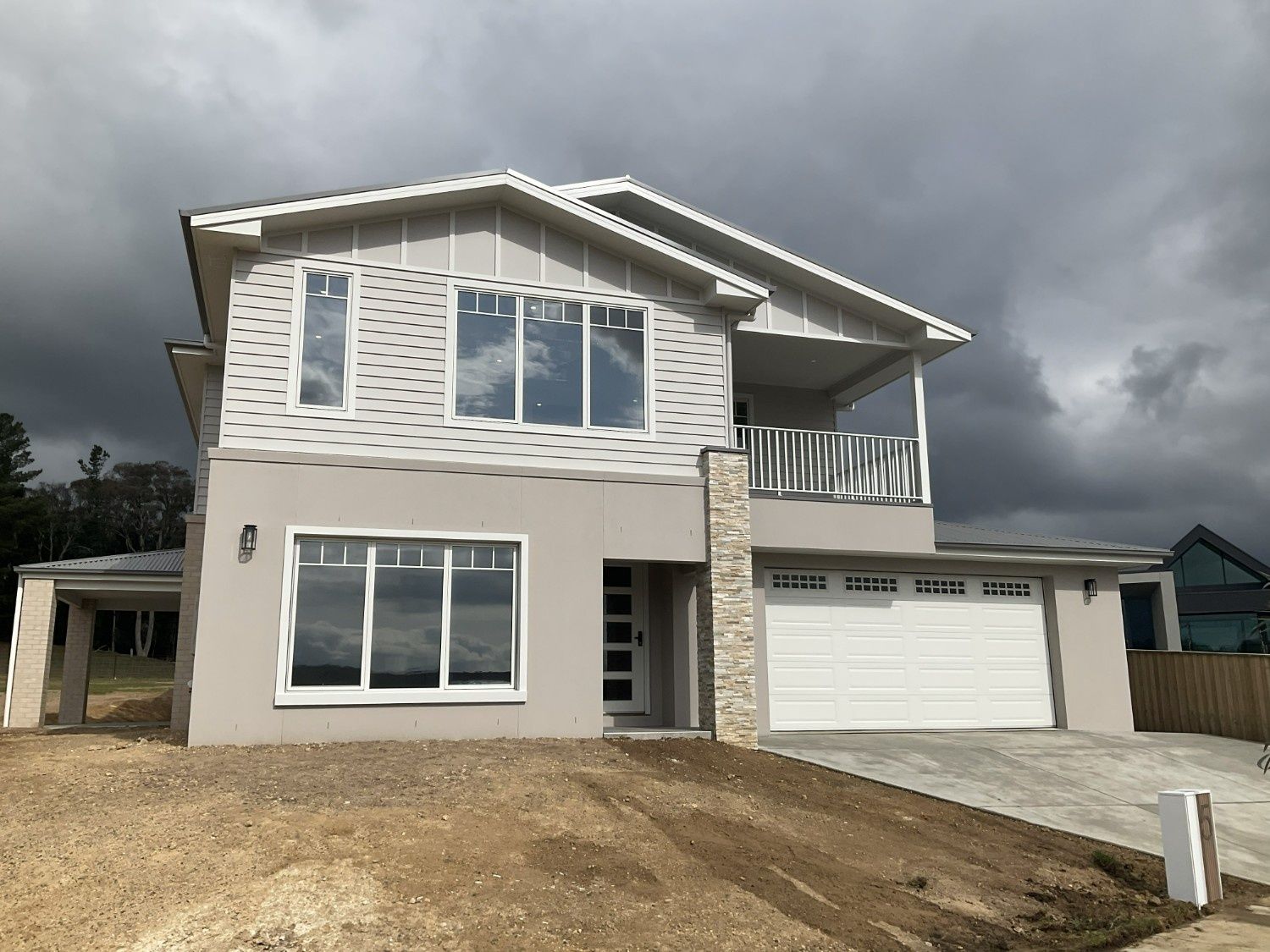 Modern two-story house with beige siding, large windows, garage, and cloudy sky above — Twomey Homes in Delacombe, VIC