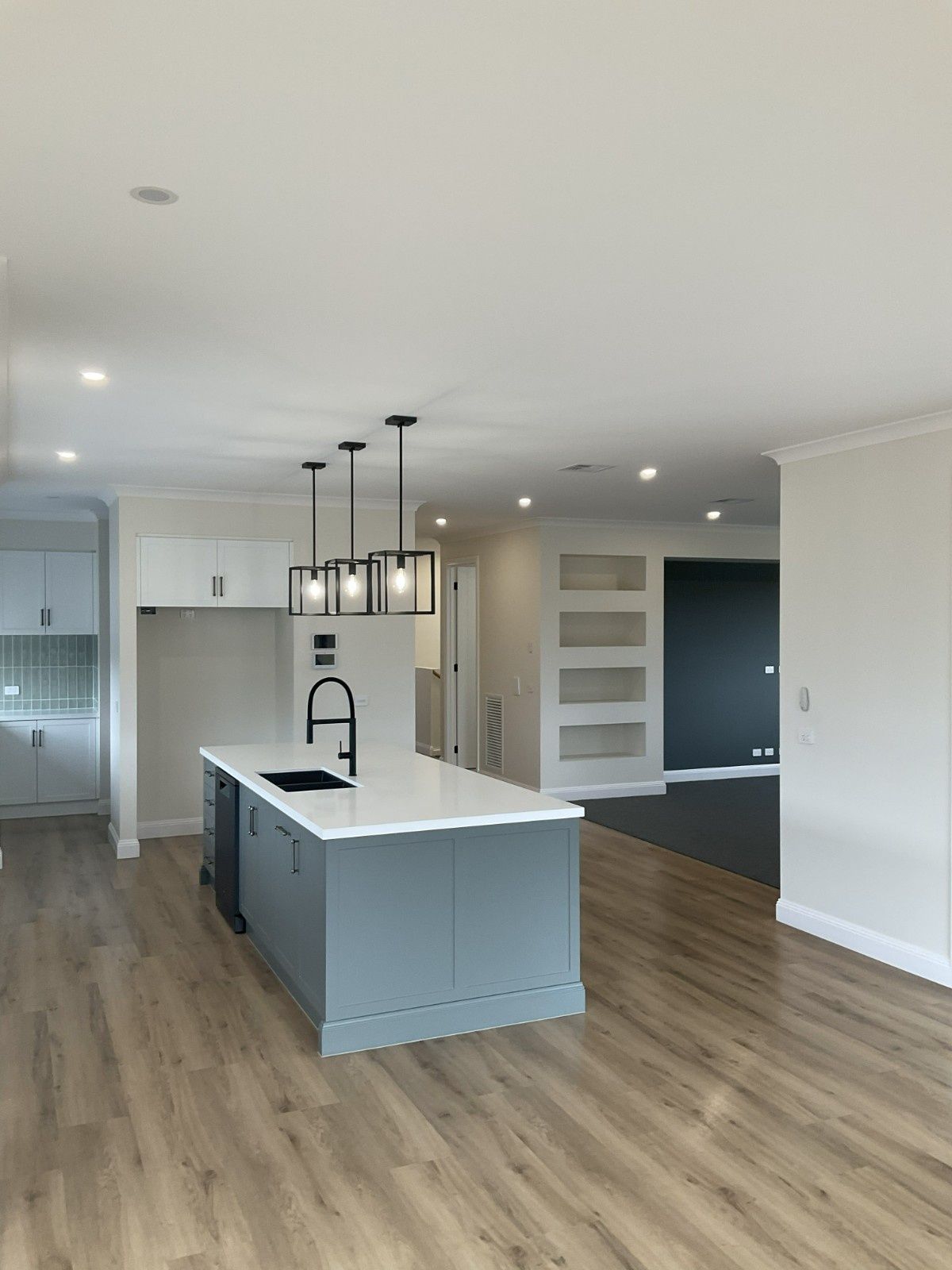 Bright modern kitchen and living area with island, pendant lights, grey cabinets, and wood floors — Twomey Homes in Delacombe, VIC