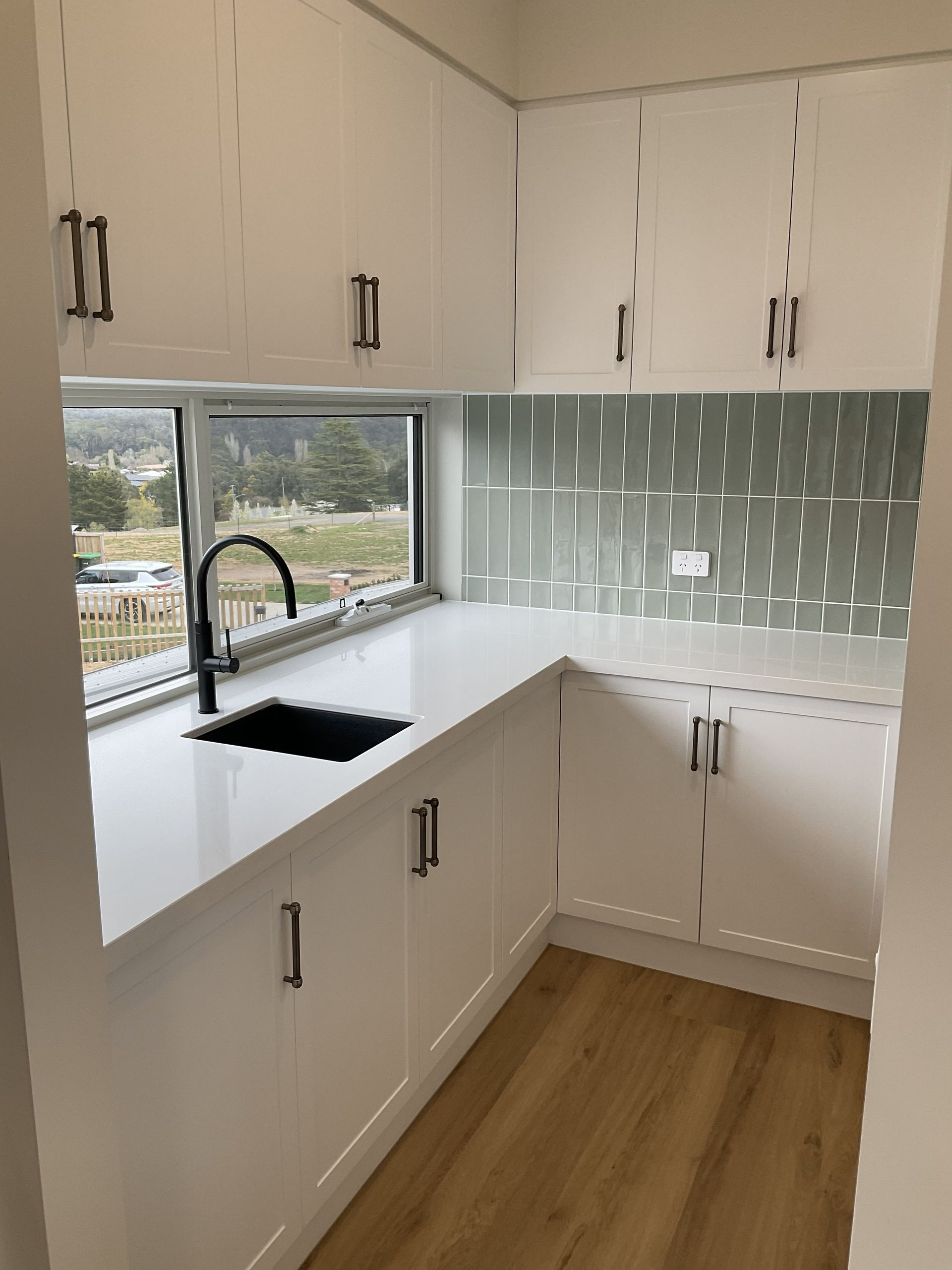 Bright white kitchen with L-shaped counters, pale green tile backsplash, and window over sink — Twomey Homes in Delacombe, VIC