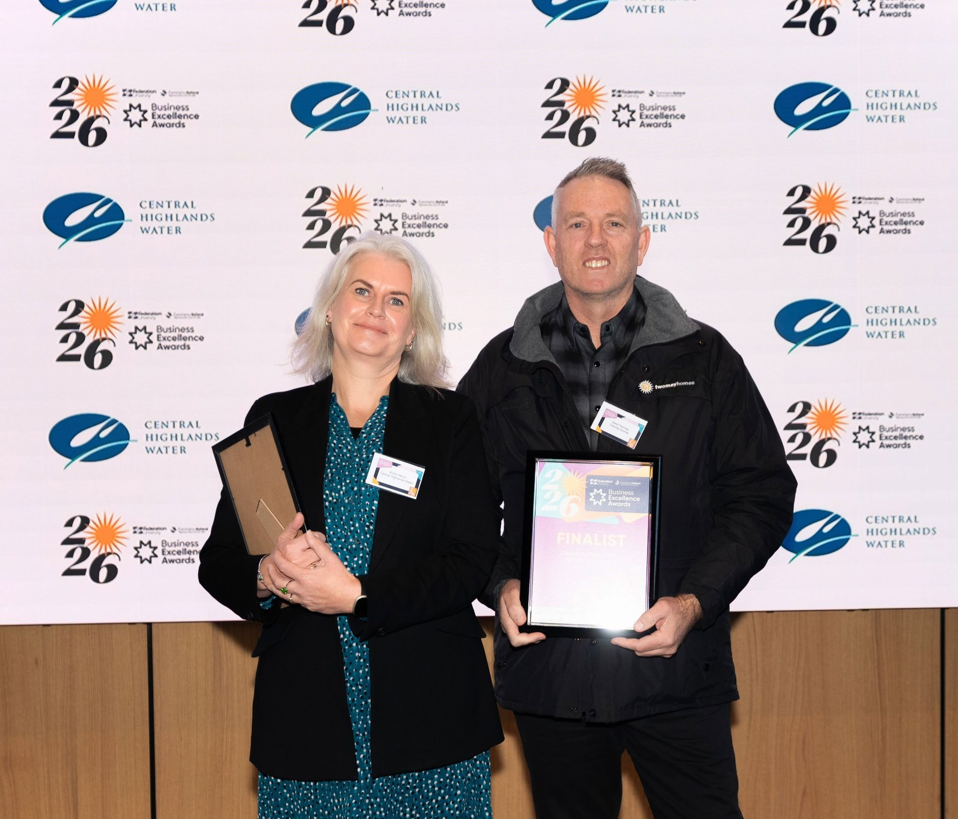 Two people holding plaques pose in front of a branded event backdrop — Twomey Homes in Delacombe, VIC