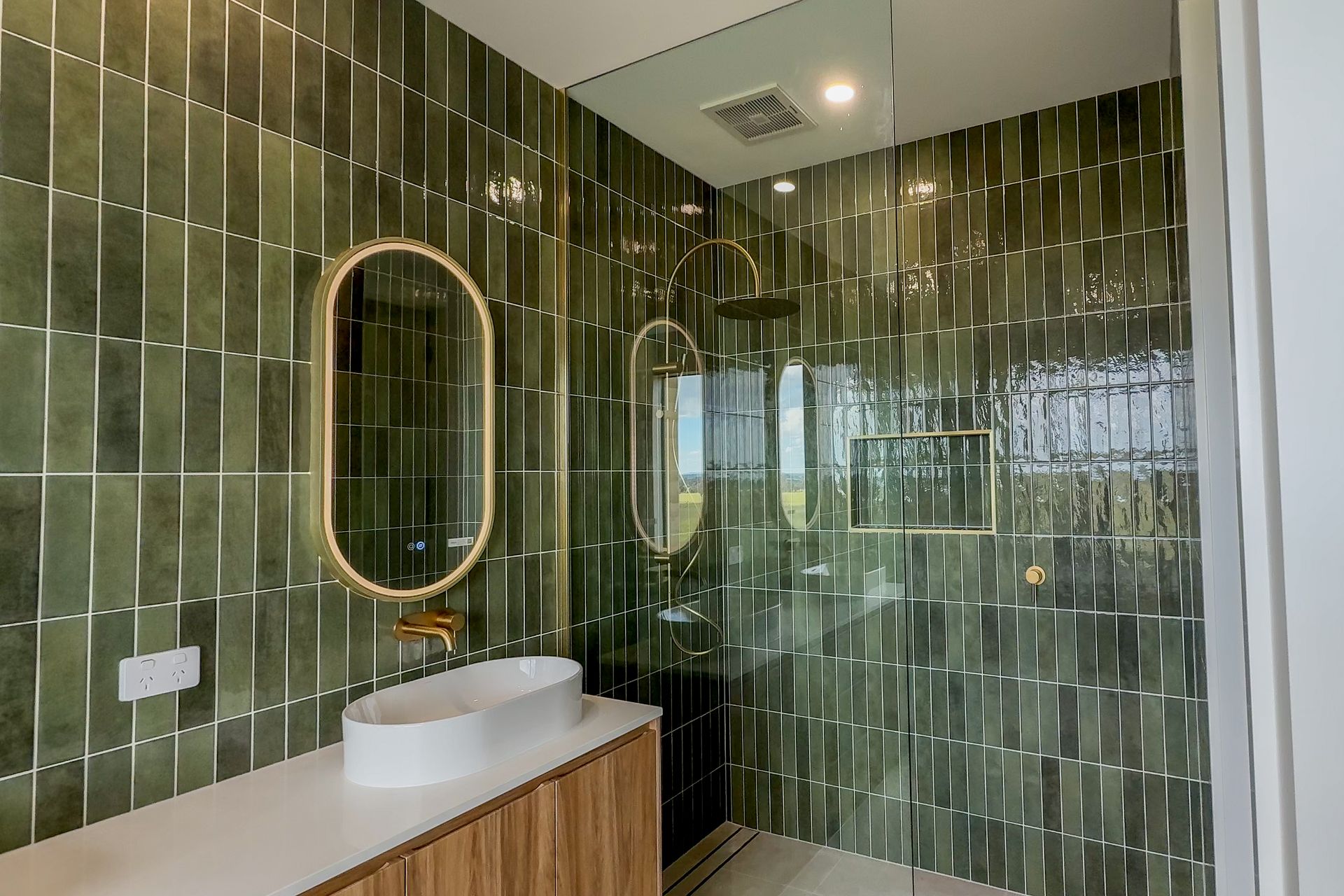 Modern bathroom with green tiled walls, oval mirror, and white vessel sink on a wood vanity — Twomey Homes in Delacombe, VIC