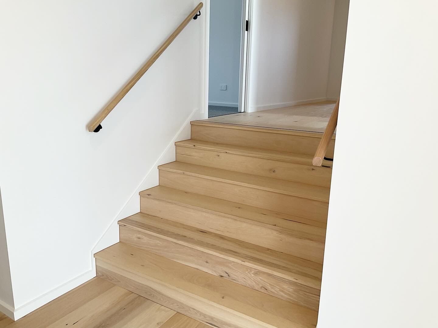 Wooden staircase with a light wood handrail in a white interior hallway — Twomey Homes in Delacombe, VIC