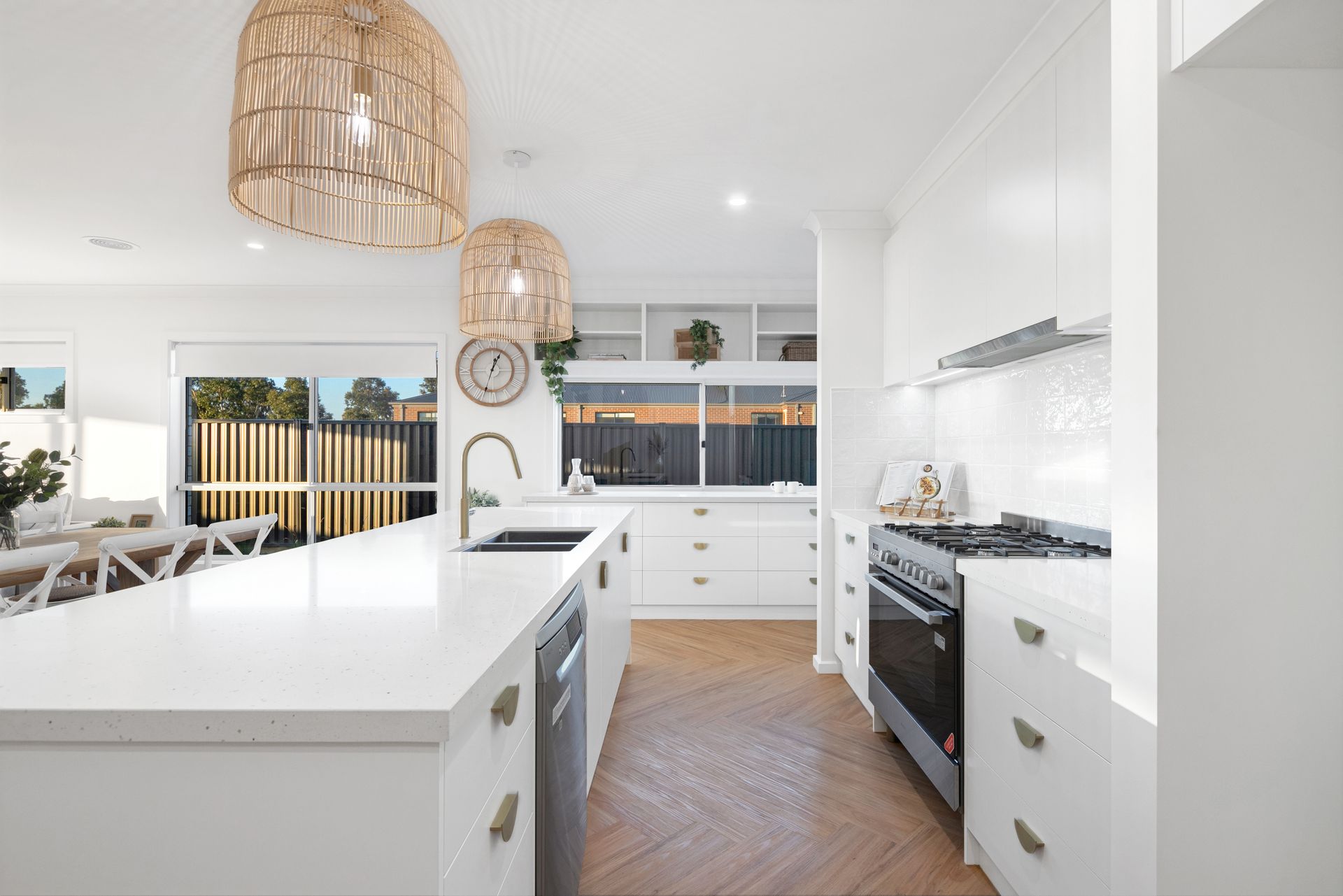 Bright modern white kitchen with island, pendant lights, black stove, and herringbone wood floor — Twomey Homes in Delacombe, VIC