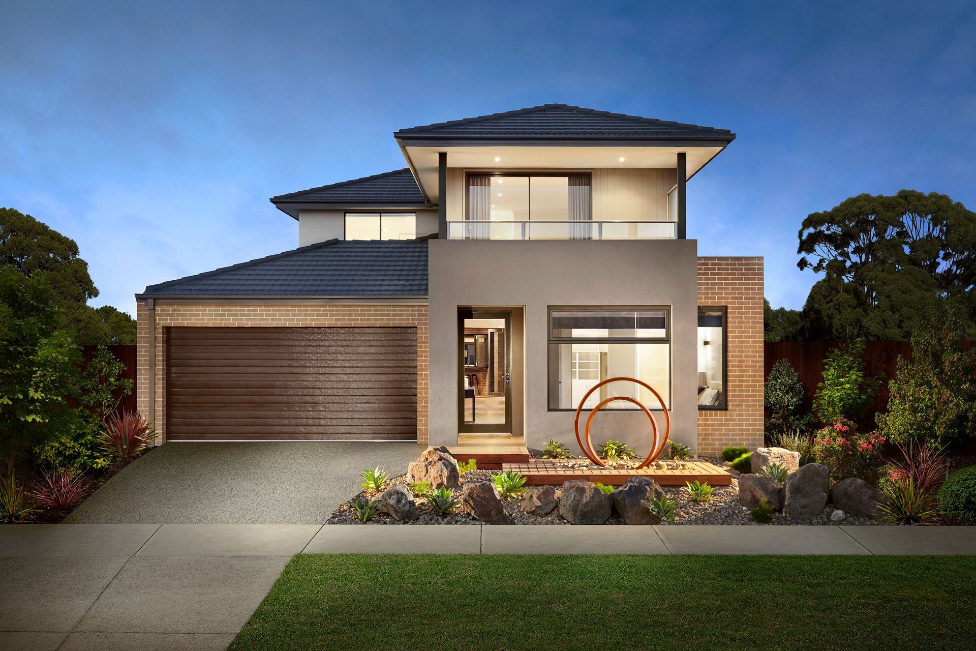 Modern two-story house with a garage, landscaped front yard, and lit entry at dusk — Twomey Homes in Delacombe, VIC