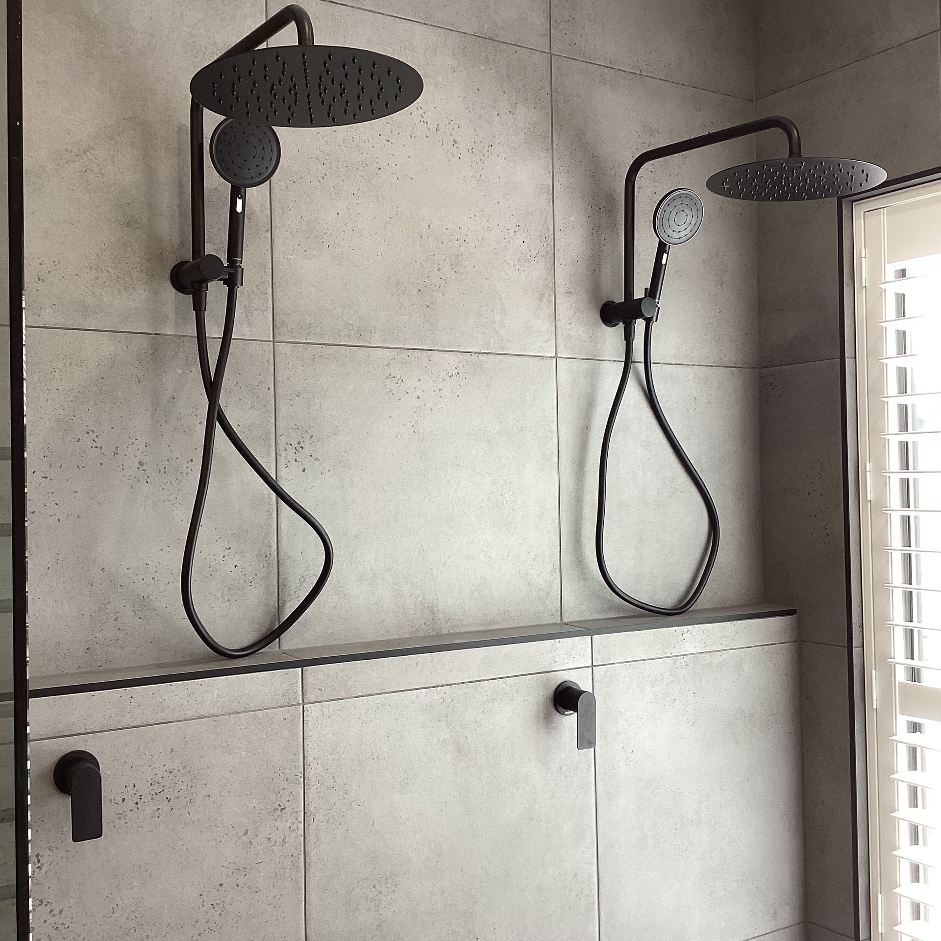 Modern shower stall with two black rainfall showerheads and a frosted glass door — Twomey Homes in Delacombe, VIC