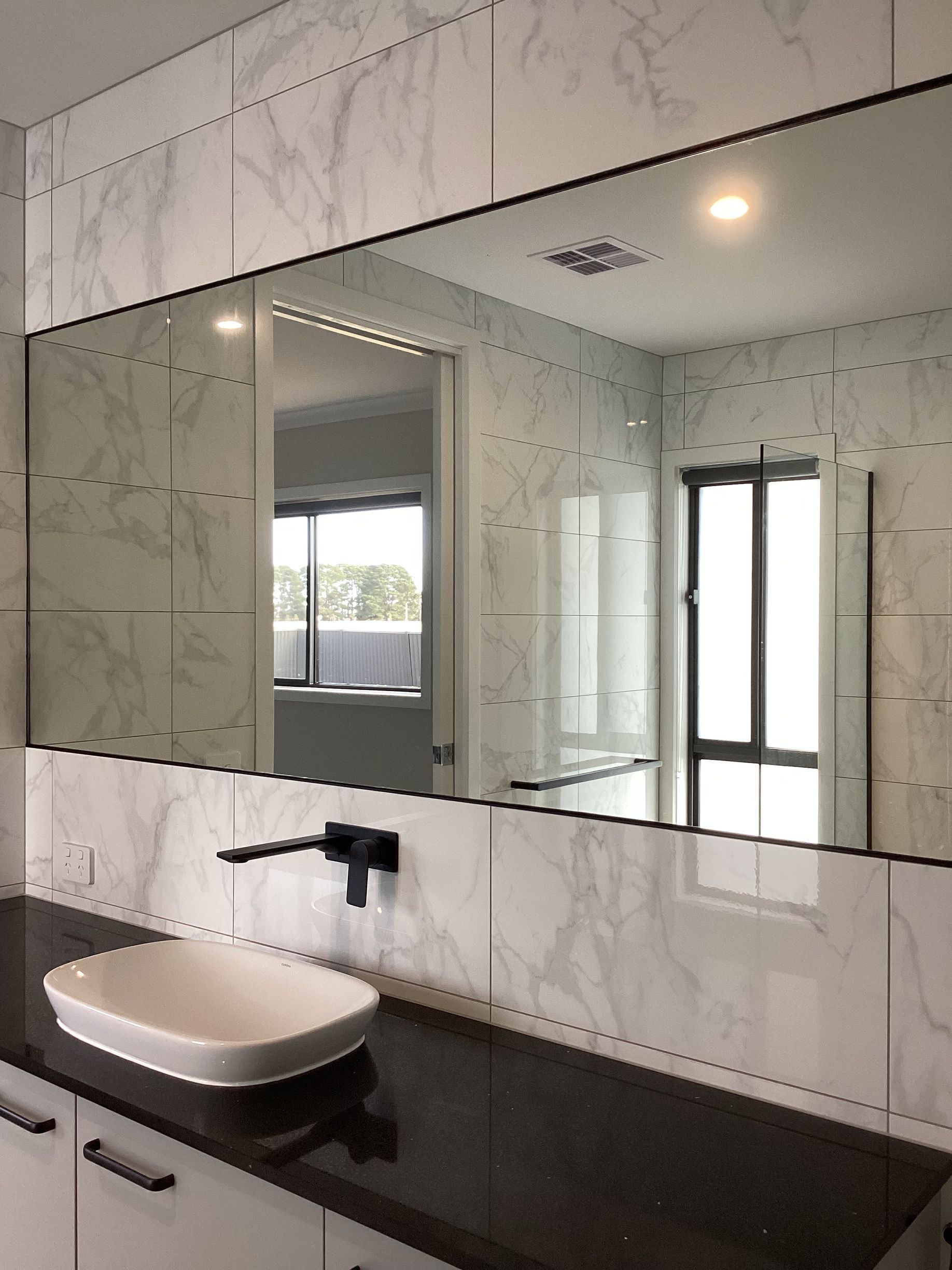 Modern bathroom vanity with white vessel sink, black countertop, and large wall mirror — Twomey Homes in Delacombe, VIC
