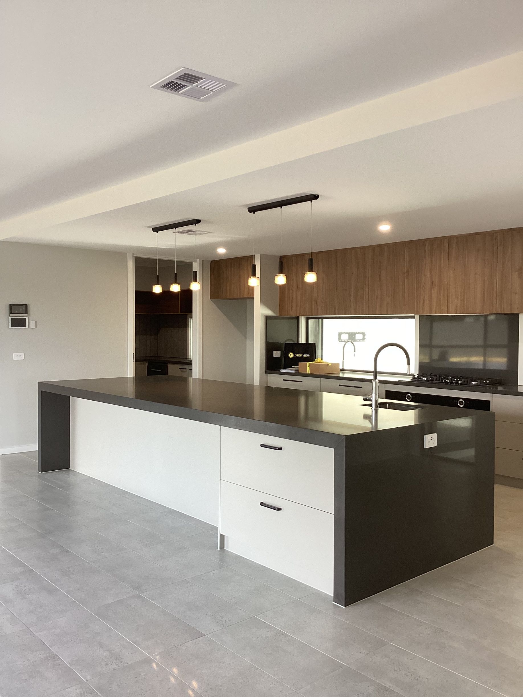 Modern kitchen with large island, dark cabinetry, wood accents, and grey tiled floor — Twomey Homes in Delacombe, VIC