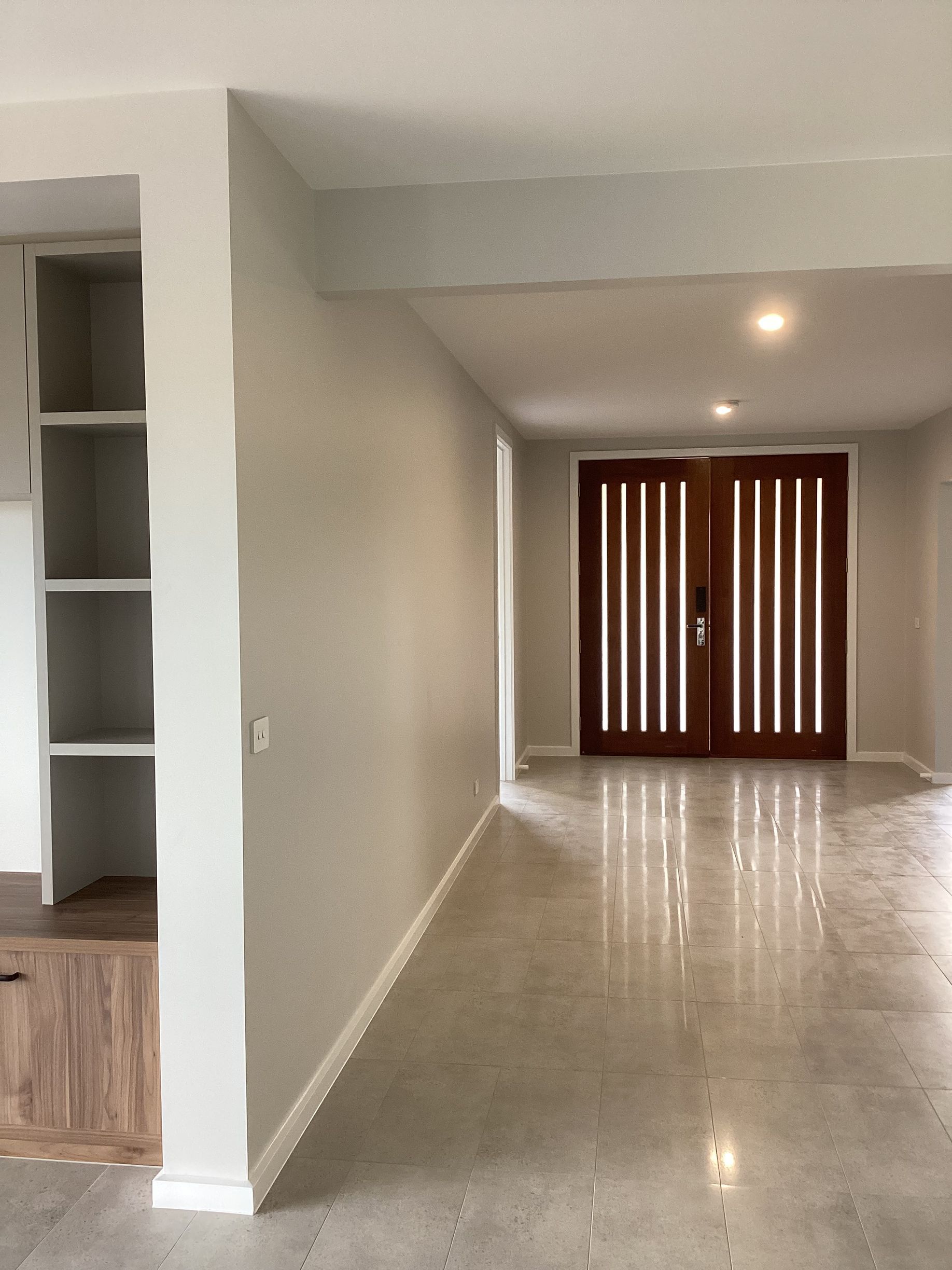 Empty modern hallway with glossy tile floor, white walls, built-in shelves, and wooden front doors at the end — Twomey Homes in Delacombe, VIC