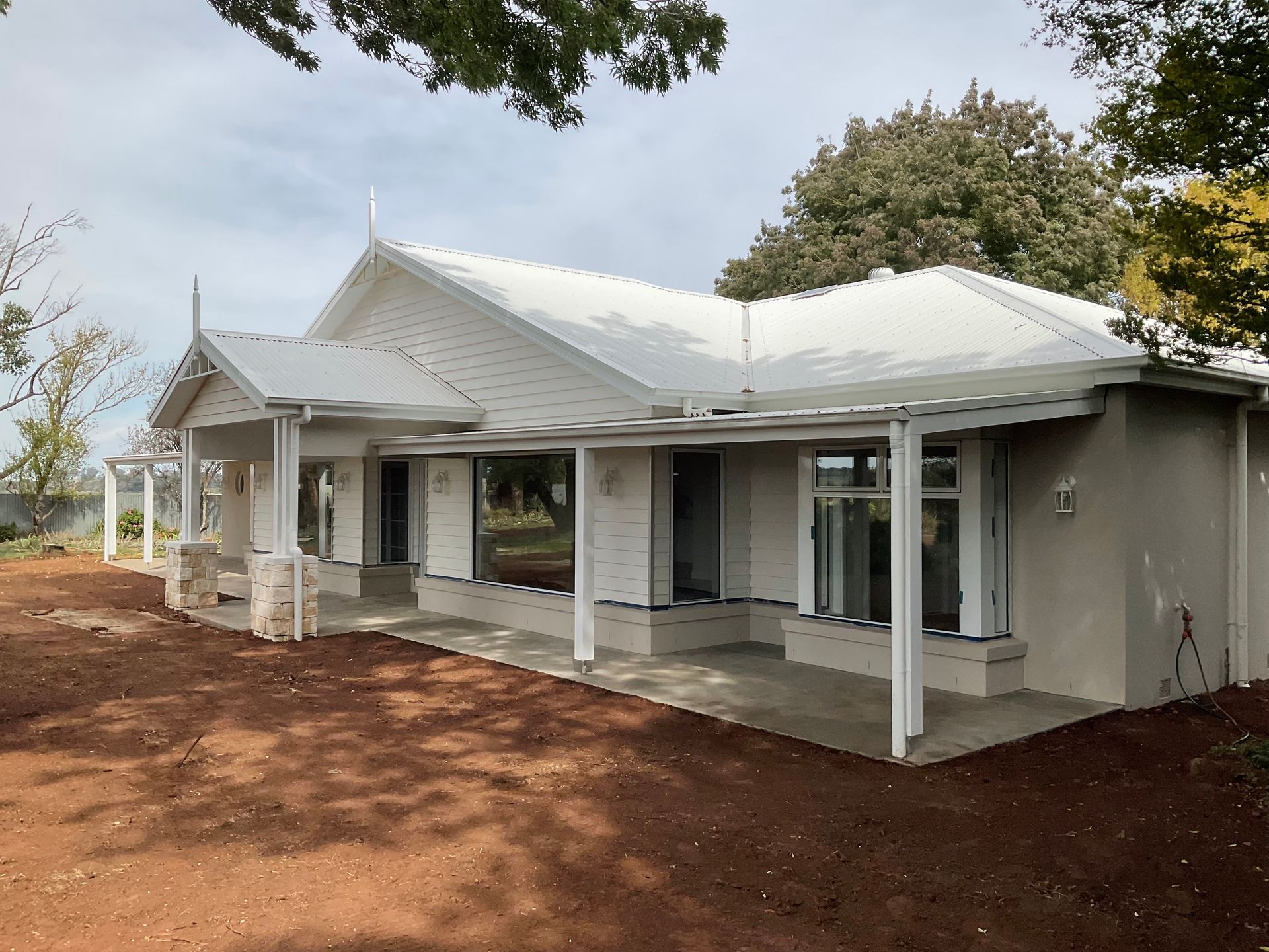 White single-story house with a covered porch and grey trim, set on red dirt under cloudy skies — Twomey Homes in Delacombe, VIC