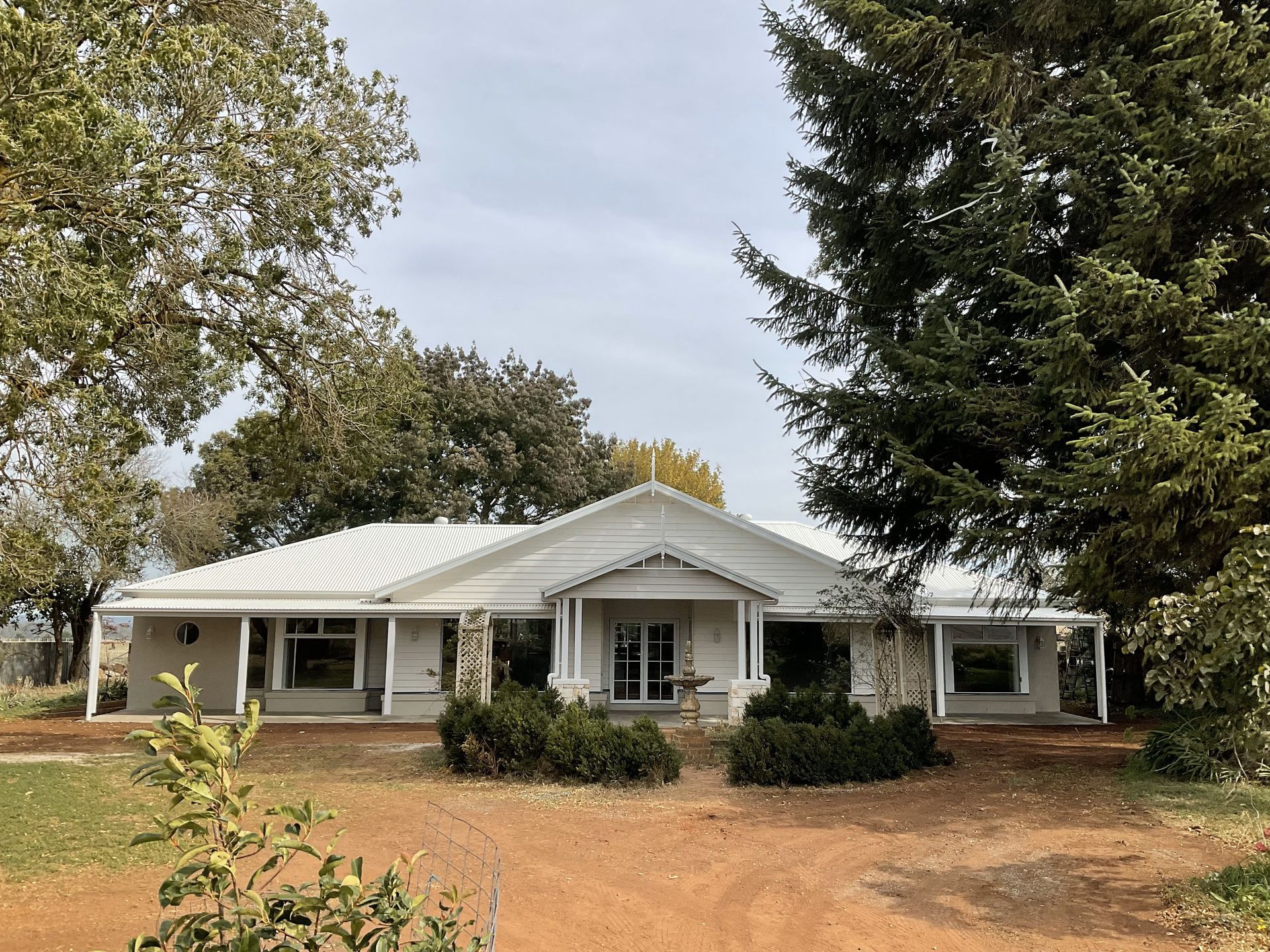 Single-story white farmhouse with a front porch, surrounded by trees and dry yard — Twomey Homes in Delacombe, VIC