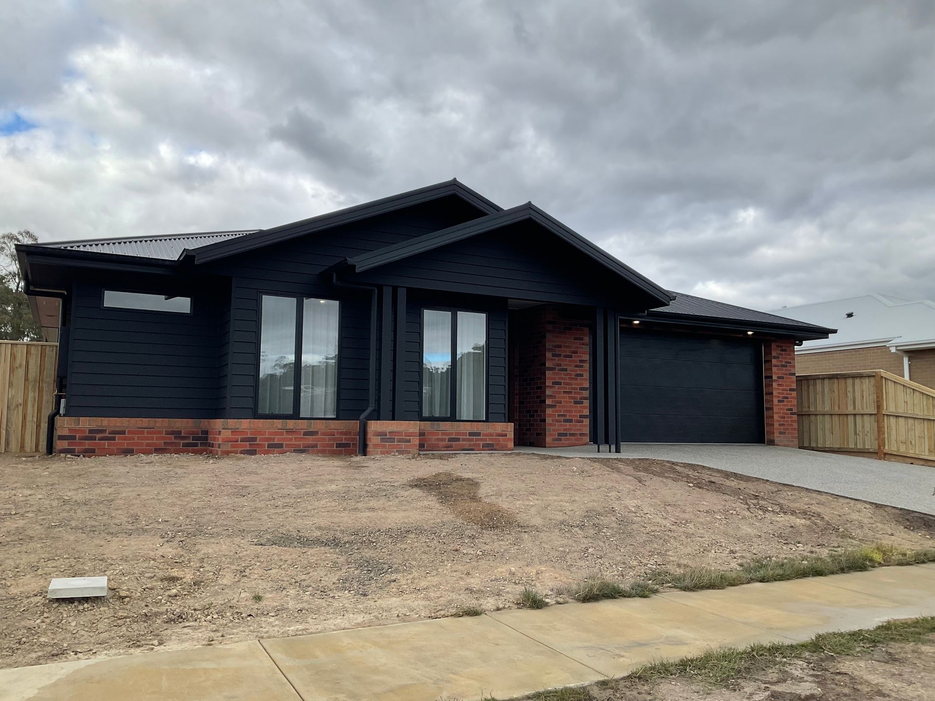 Modern black house with red brick accents and a garage, viewed from the front under cloudy skies — Twomey Homes in Delacombe, VIC