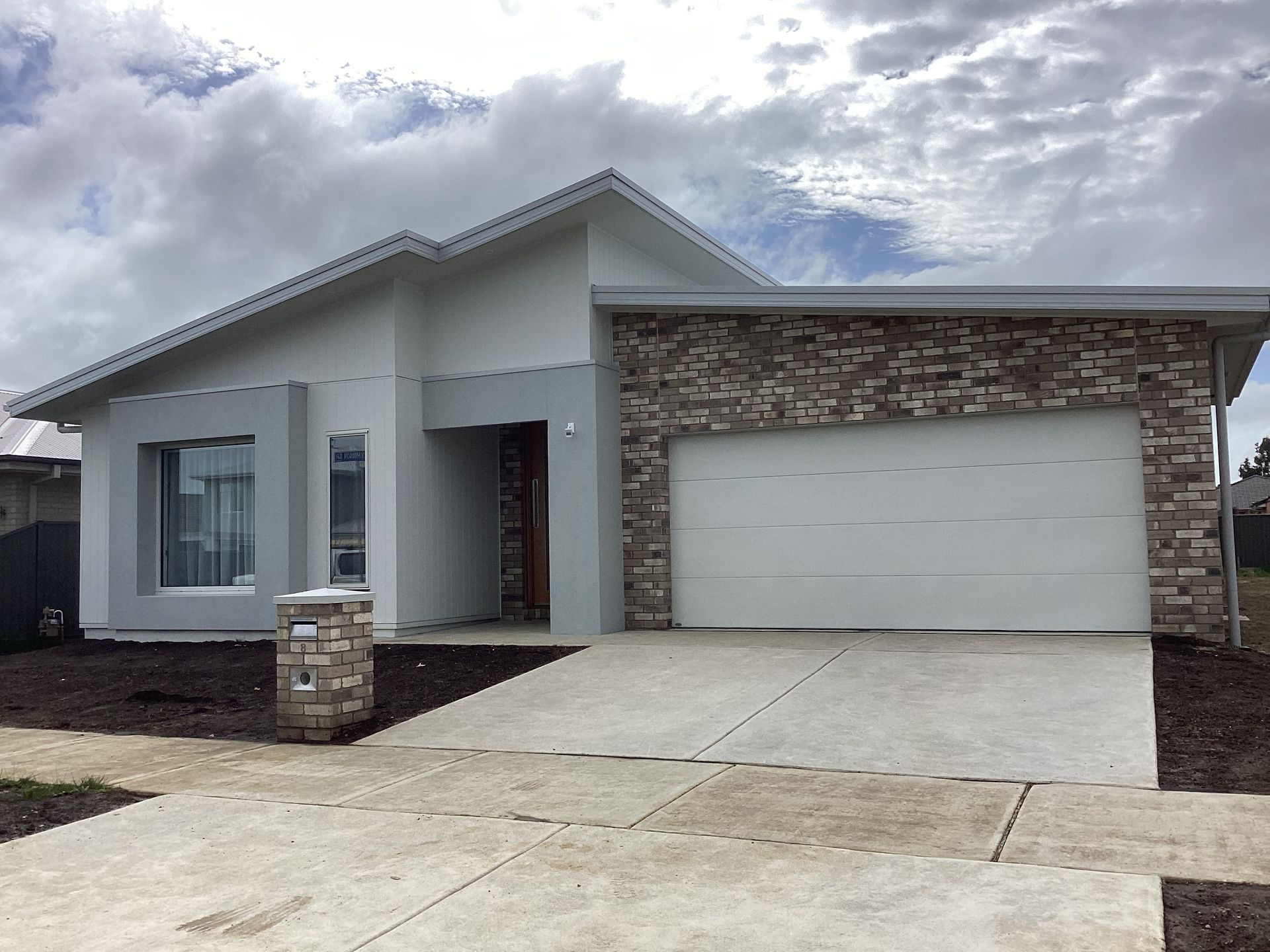 Modern single-story house with stone facade, white garage door, and cloudy sky — Twomey Homes in Delacombe, VIC