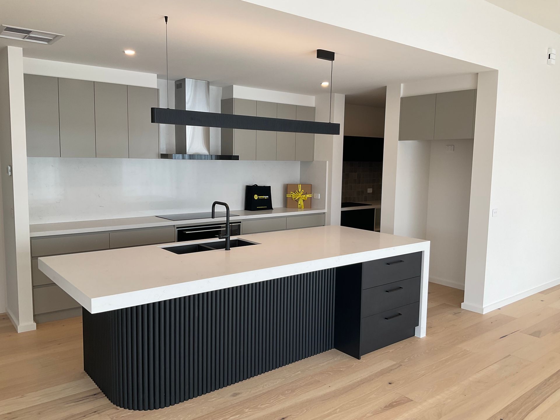 Modern kitchen with white island, dark front panel, light wood floors, and grey cabinetry — Twomey Homes in Delacombe, VIC