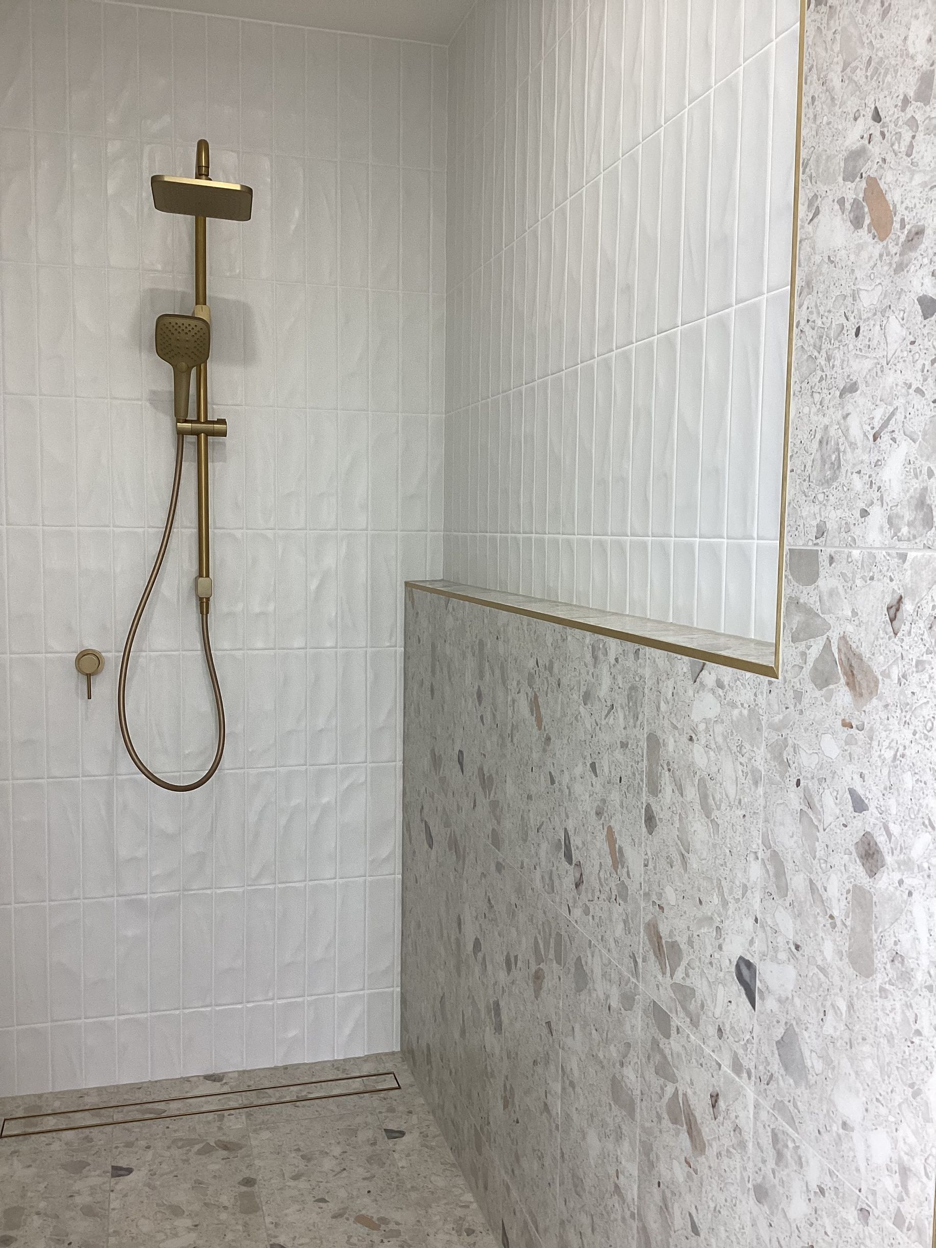 Small tiled shower with a brass cross-shaped shower fixture and a handheld showerhead — Twomey Homes in Delacombe, VIC
