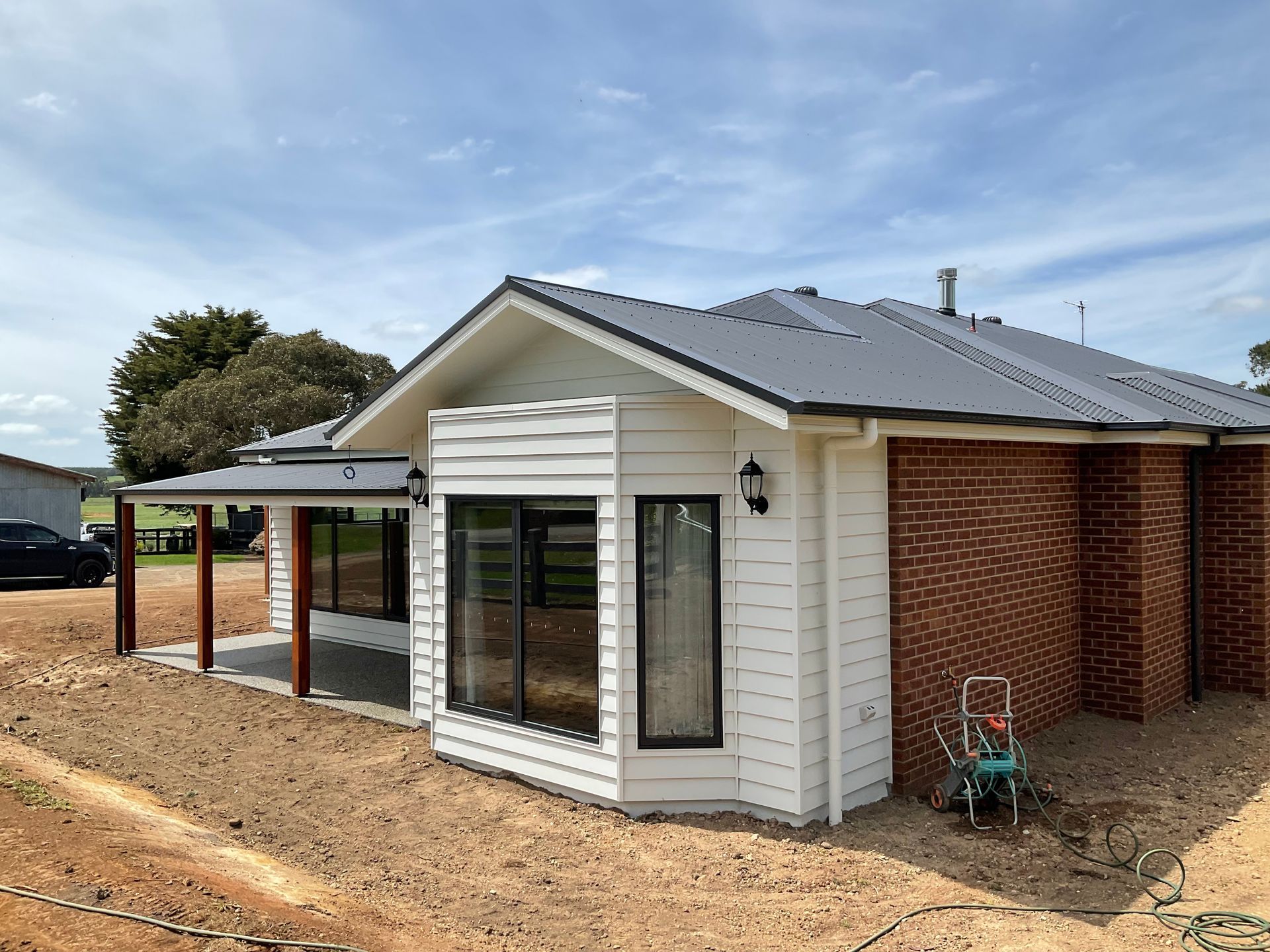 Modern white house with brick walls, grey roof, and a covered patio on a dirt lot — Twomey Homes in Delacombe, VIC