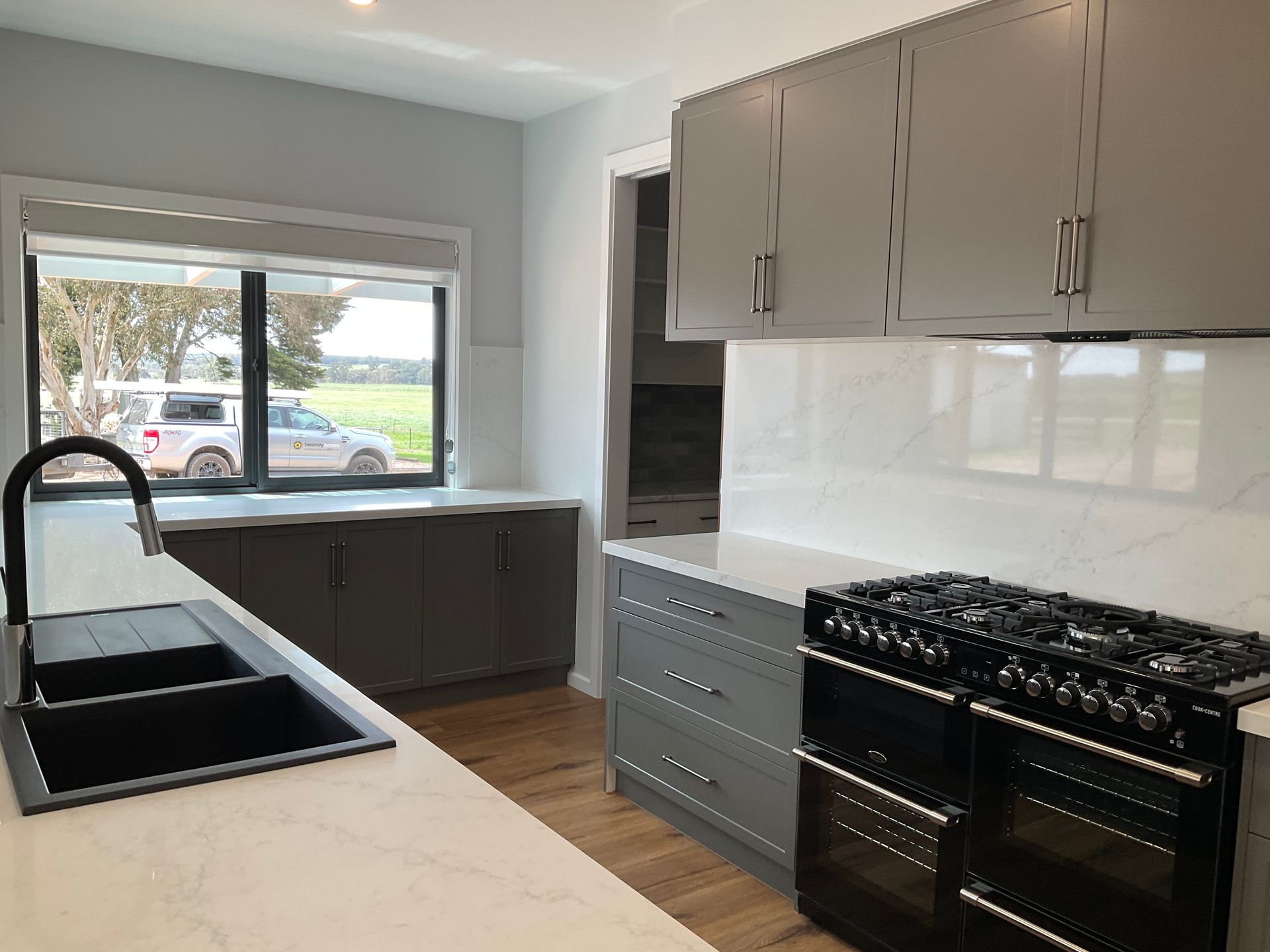 Modern kitchen with white cabinets, black sink, gas range, and large window over a counter — Twomey Homes in Delacombe, VIC
