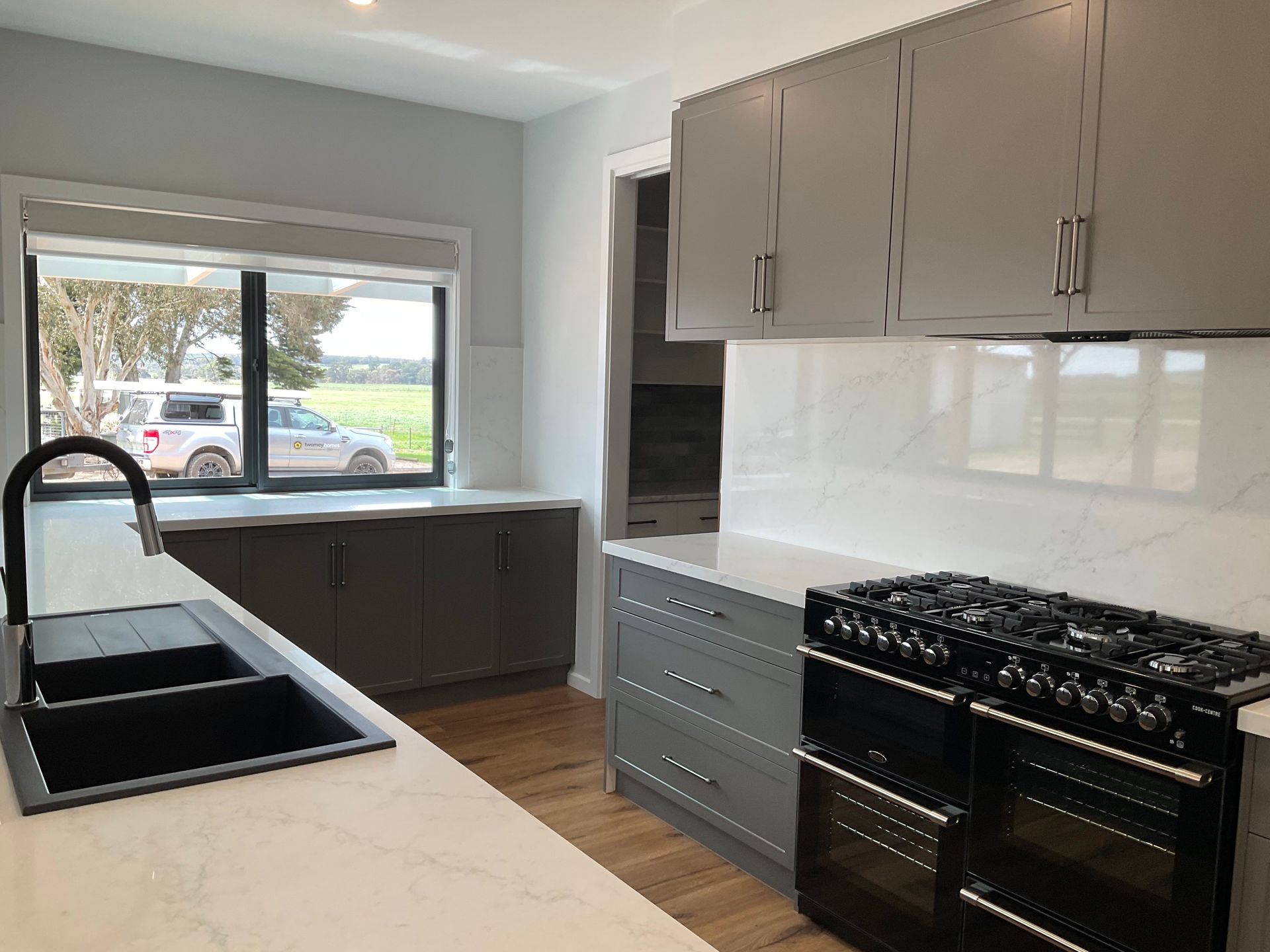 Modern kitchen with black sink, white cabinets, and a gas range by a large window — Twomey Homes in Delacombe, VIC