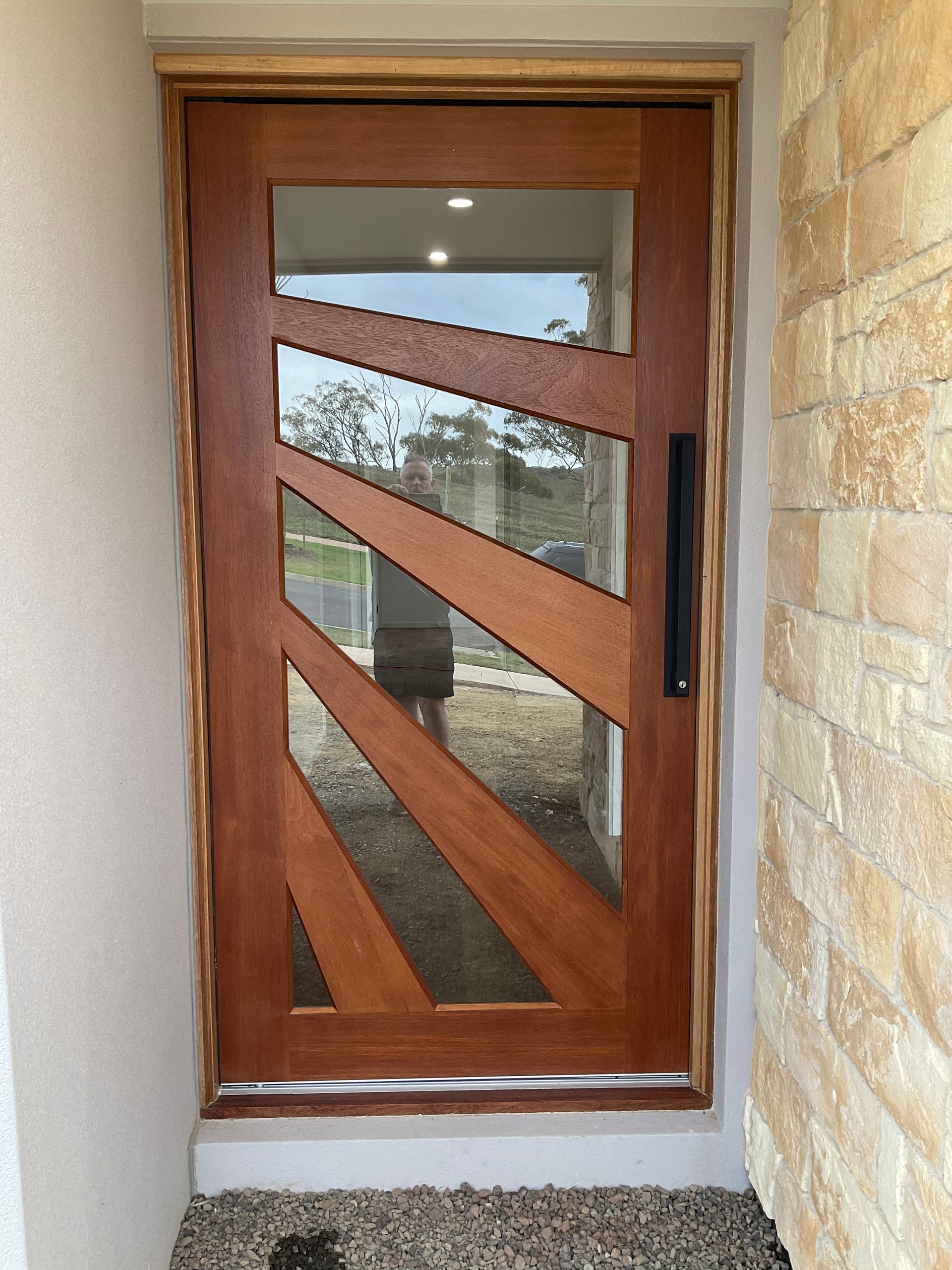 Wooden front door with diagonal frosted-glass panels framed by brick and stucco walls — Twomey Homes in Delacombe, VIC