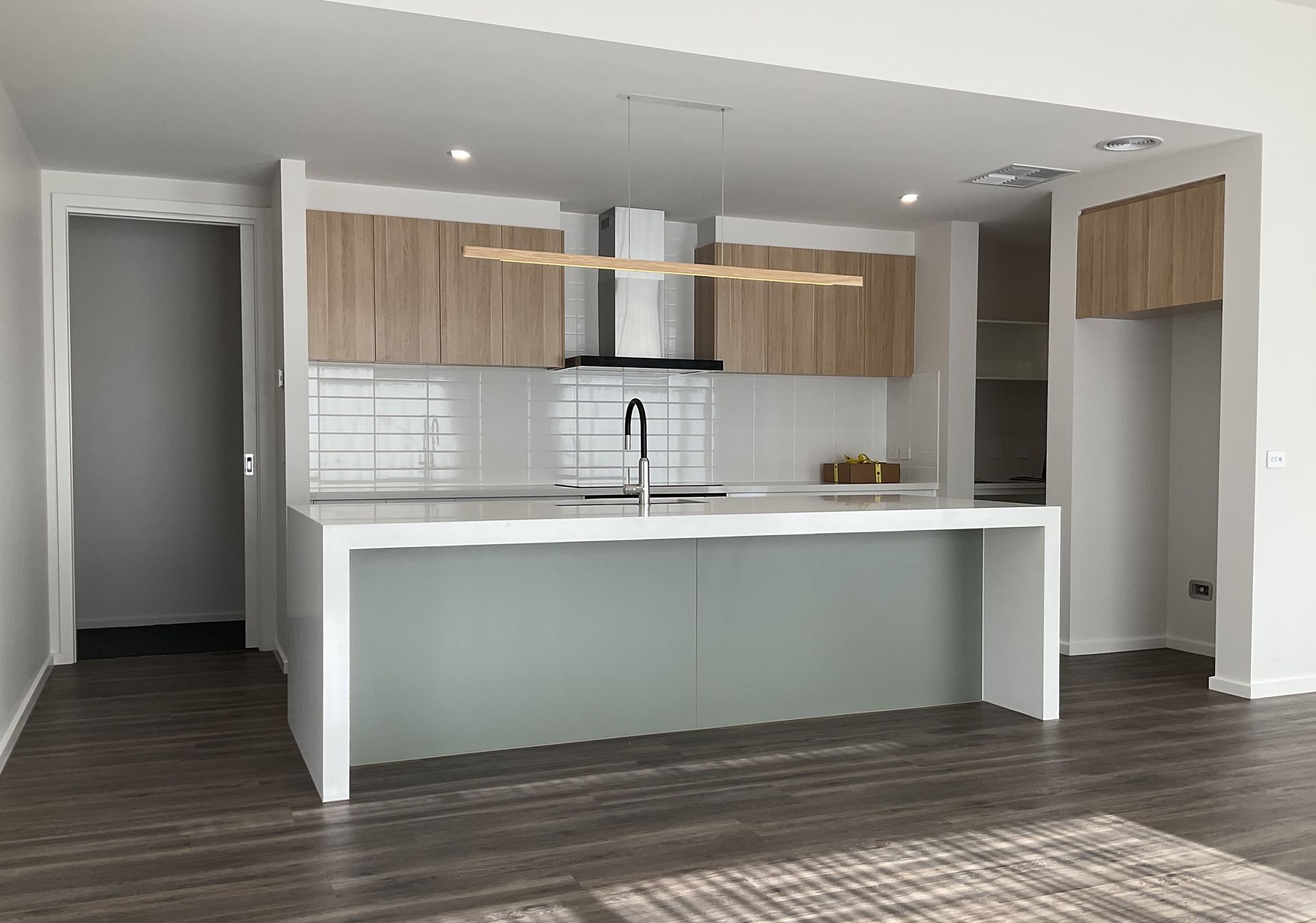 Modern kitchen with white island, wood cabinets, and stainless steel appliances — Twomey Homes in Delacombe, VIC