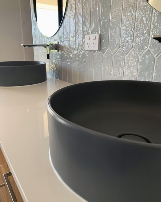 Modern bathroom vanity with black vessel sinks, oval mirror, and tiled wall — Twomey Homes in Delacombe, VIC
