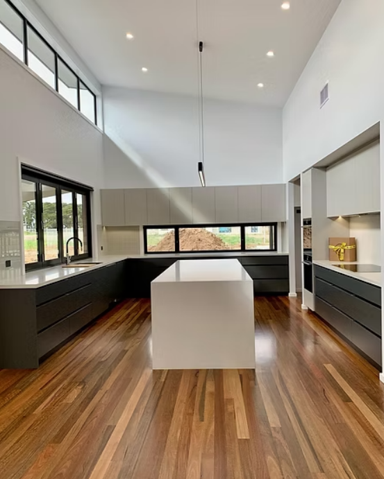 Modern kitchen with dark cabinets, white island, tall windows, and wood floors — Twomey Homes in Delacombe, VIC