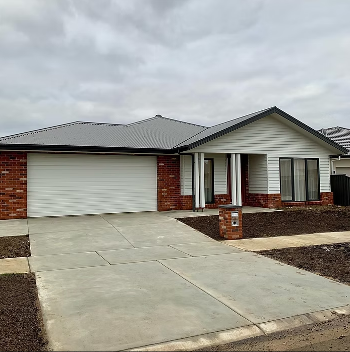 Single-story suburban house with white siding, red brick accents, and a two-car garage under a cloudy sky — Twomey Homes in Delacombe, VIC