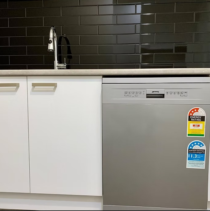 Modern kitchen with white cabinets, black tile backsplash, stainless sink and dishwasher, and black countertop — Twomey Homes in Delacombe, VIC