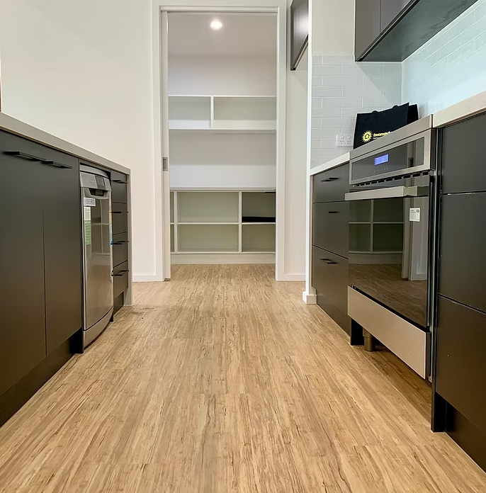 Modern kitchen hallway with black appliances, wood flooring, and a white pantry alcove — Twomey Homes in Delacombe, VIC