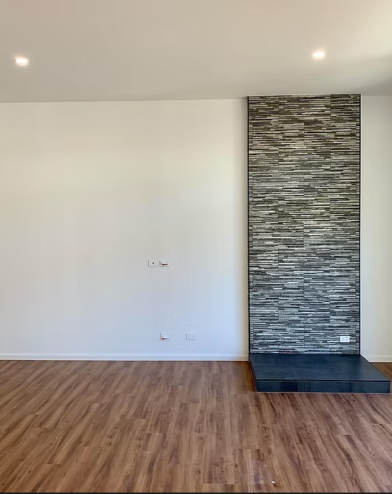 Empty modern room with wood flooring, white walls, and a tall stone accent fireplace or column — Twomey Homes in Delacombe, VIC